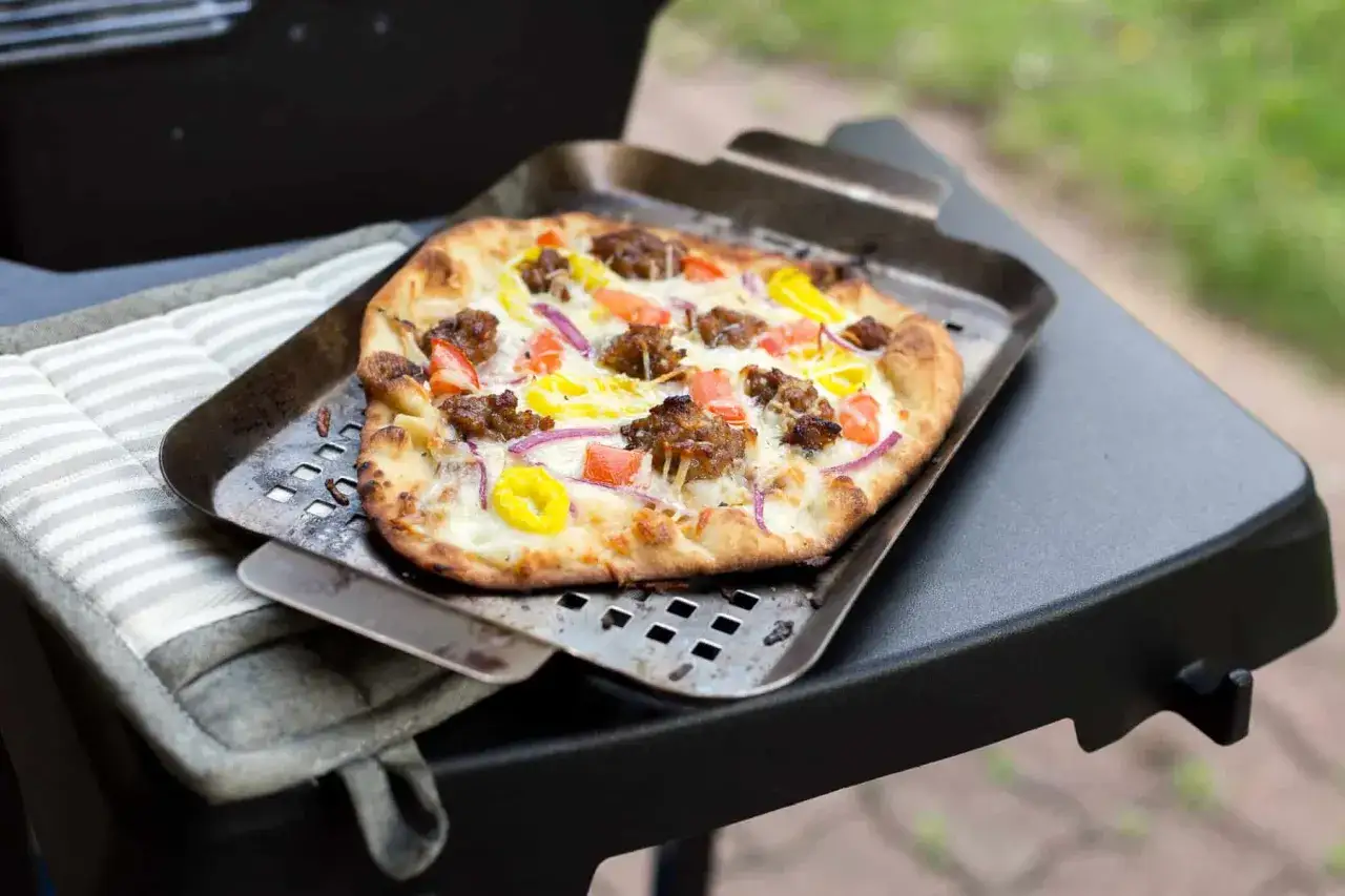 Pyszna pizza z grilla gazowego, z kawałkami kiełbasy, cebuli i papryki, na metalowej łopatce.