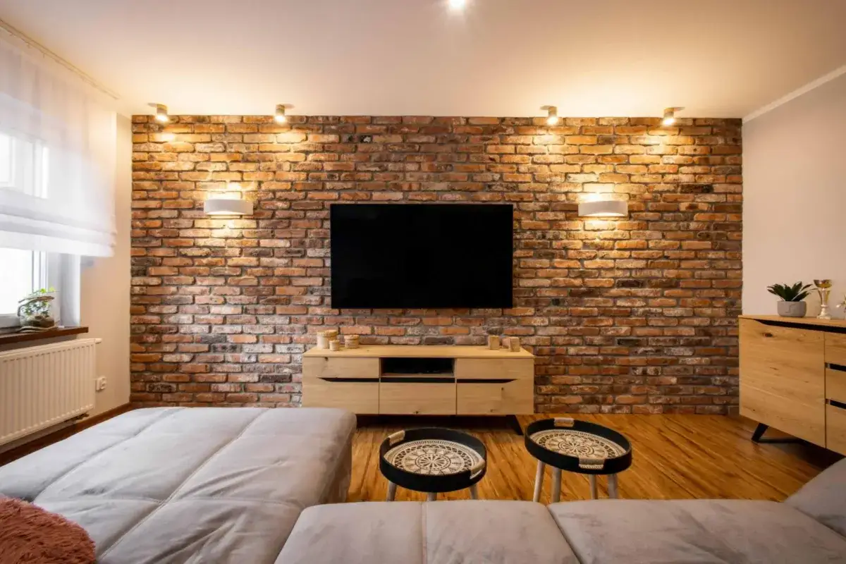 Nowoczesny salon z ceglaną ścianą, telewizorem i wygodną kanapą. Zastanawiasz się, ile jest warte mieszkanie w bloku z takim wnętrzem?