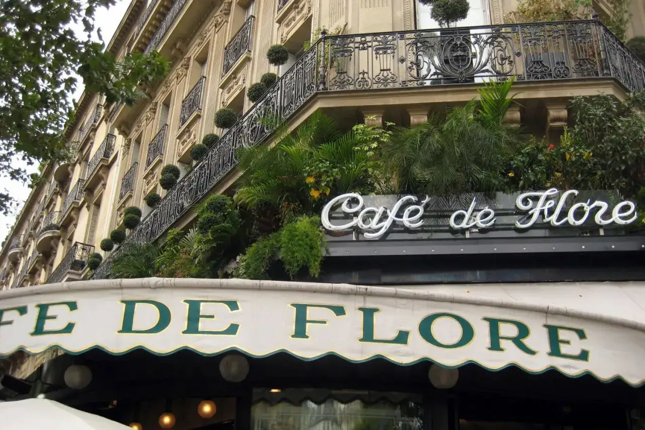 Elegancka fasada kawiarni Café de Flore w 6 dzielnicy Paryża, ozdobiona bujną zielenią i kutymi balustradami.