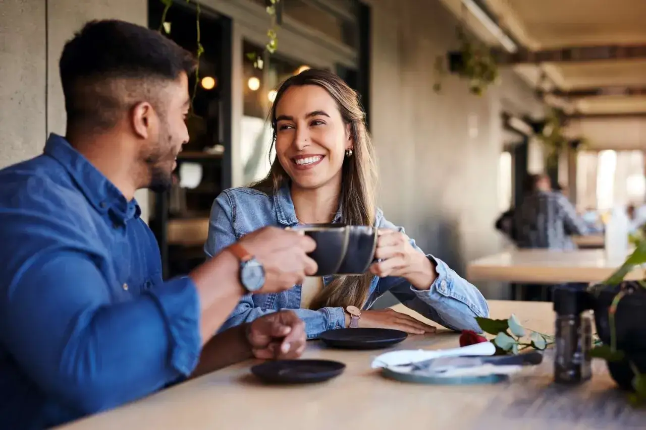 Para na randce, uśmiechnięta kobieta podaje mężczyźnie kawę. Rozmowa toczy się płynnie, jakby wymieniali pytania na randkę.