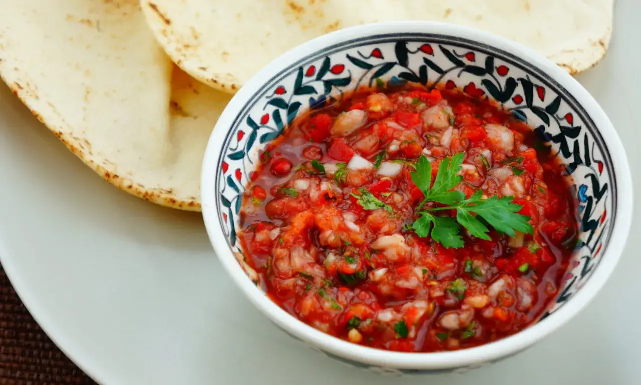 Miseczka z oryginalnym tureckim sosem do kebaba, pełnym pomidorów i ziół, obok ciepłych placków pita.