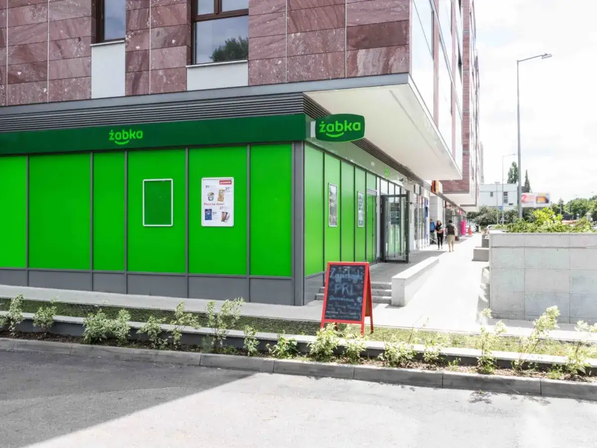Sklep Żabka z zielonymi witrynami. Na czerwonej tablicy informacja 