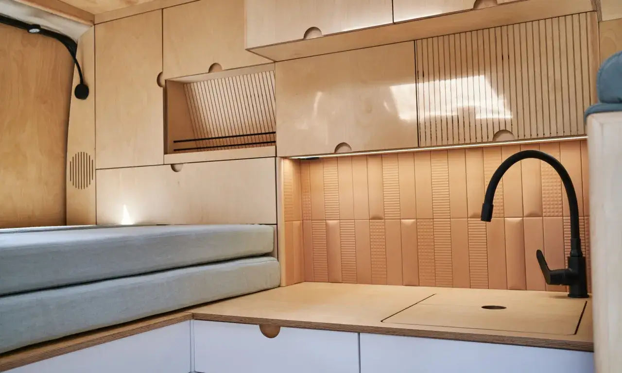 Wnętrze kampera tanio: ł&oacute;żko, drewniane szafki, zlew z czarną baterią i panel ścienny.