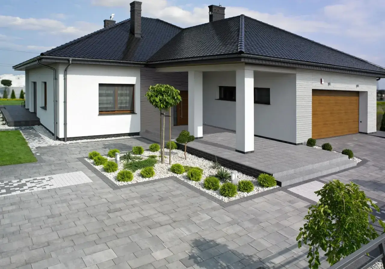 Nowoczesny dom z podjazdem i chodnikiem z szarej kostki brukowej. Inspiracje dla Twojego ogrodu i posesji.