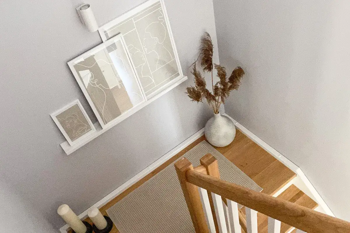 Nowoczesne, praktyczne ściany na klatce schodowej zdobią minimalistyczne grafiki i wazon z trawami.