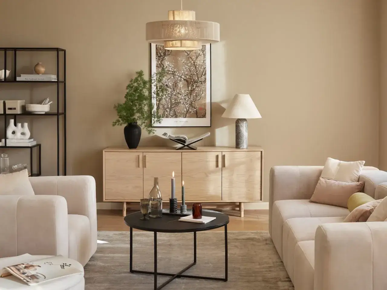 Przytulny salon z sofami w odcieniach beżu i brązu. Drewniana komoda, czarny stolik i grafika z kwitnącym drzewem tworzą harmonijną całość.