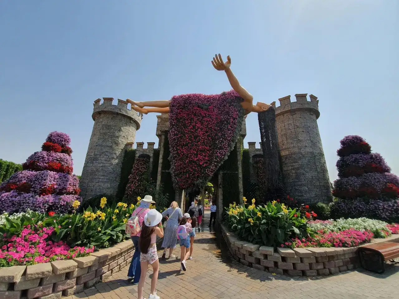 Niesamowity Miracle Garden w Dubaju: kwitnąca postać unosi się nad zamkiem z kamienia, otoczona kolorowymi kwiatami.