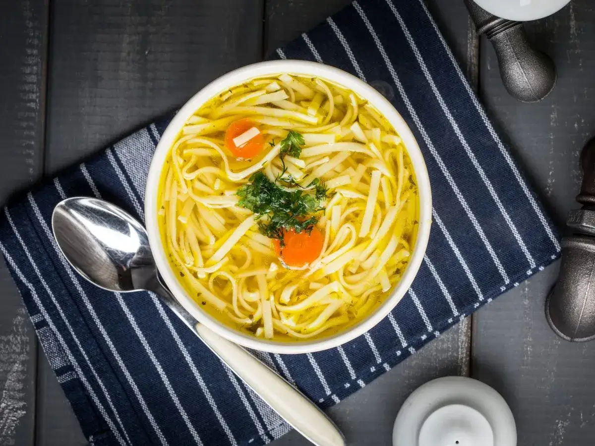 Miseczka aromatycznego rosołu z makaronem, marchewką i natką pietruszki. Idealny sposób, jak ugotować makaron do rosołu, by był pyszny.