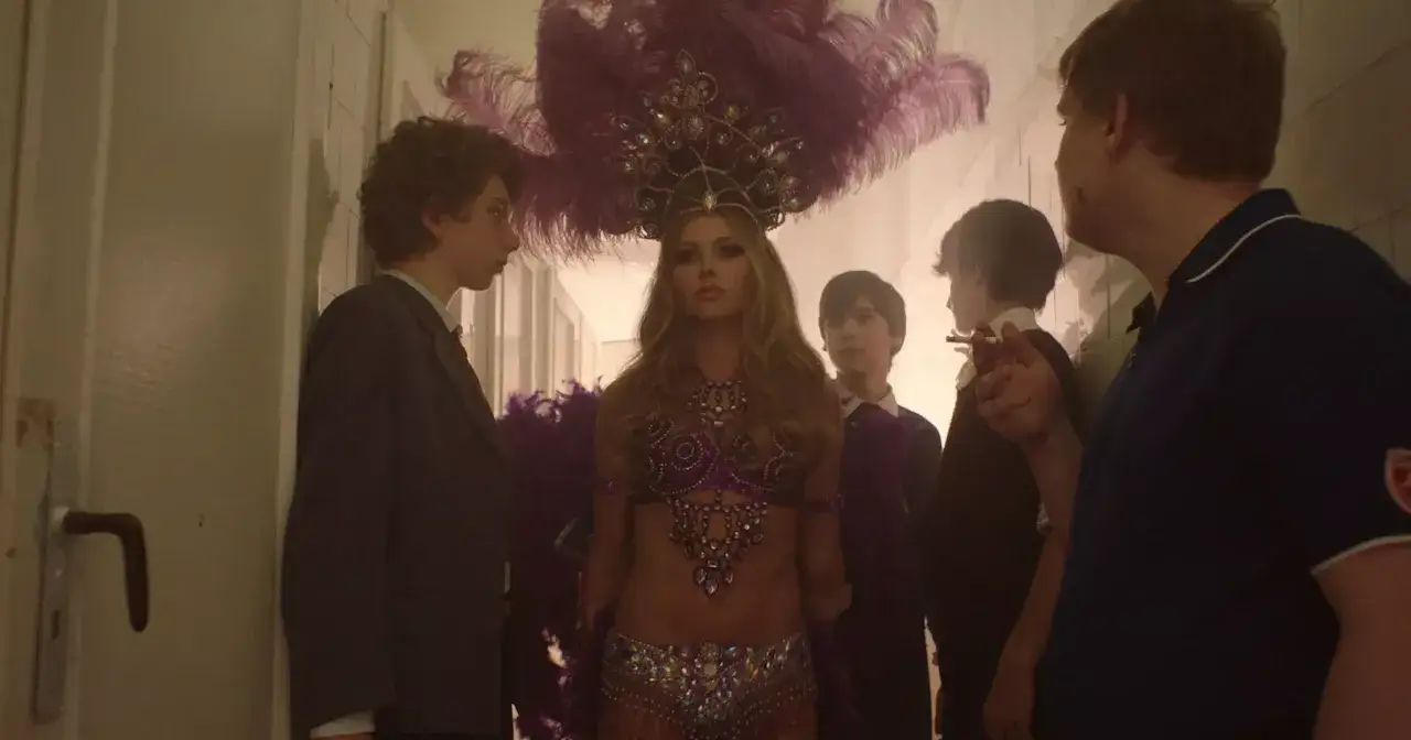 Kobieta w stroju tancerki burleski, niczym Brigitte Bardot, przygotowuje się do cudownego seansu. Otaczają ją młodzi mężczyźni.