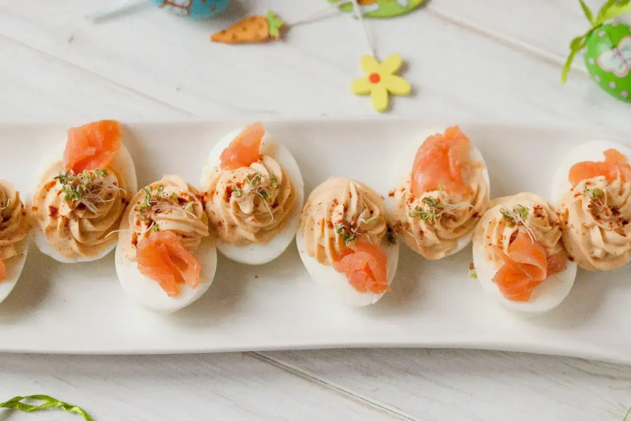 Eleganckie jajka faszerowane z łososiem, udekorowane kiełkami i papryką, idealne na wielkanocny stół.