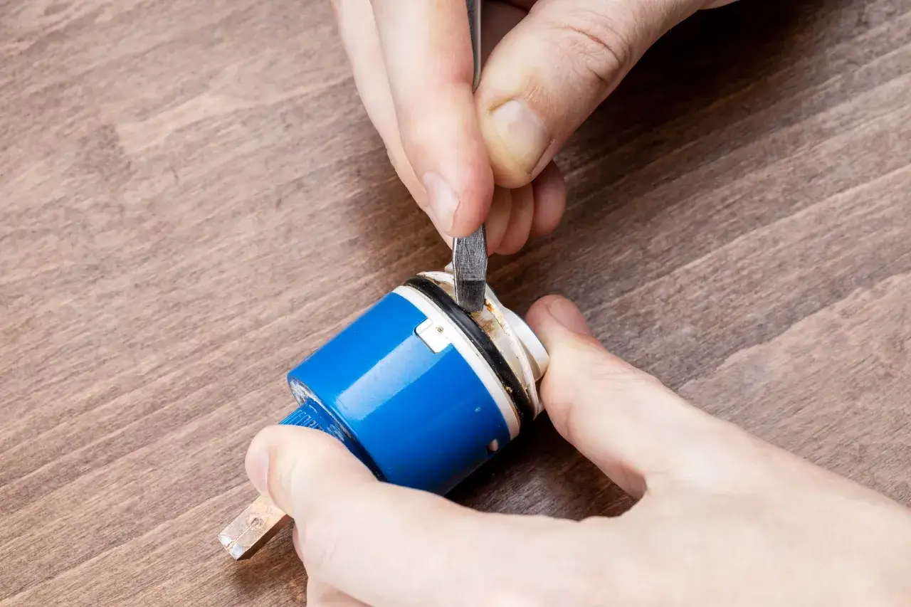 Dłonie majsterkowicza wymieniają uszczelkę do kranu, używając małego narzędzia do jej podważenia.
