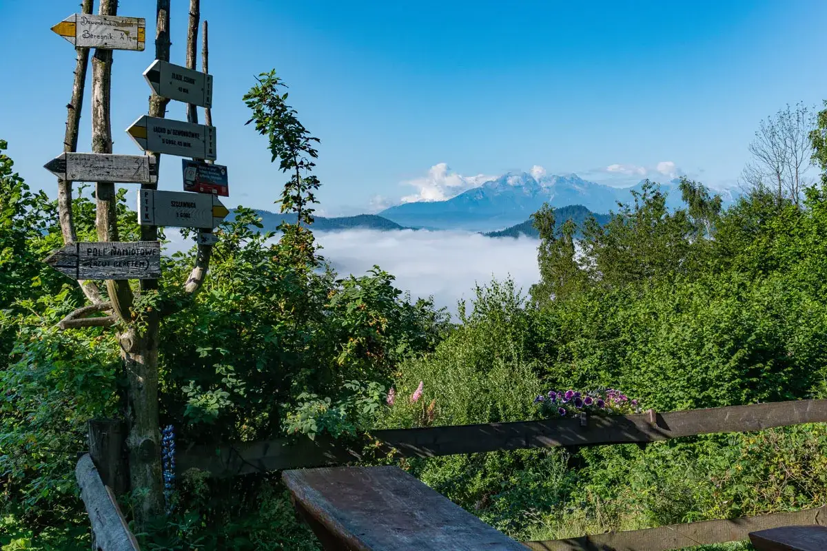 Drewniany drogowskaz PTTK pod Bereśnikiem wskazuje szlaki. W dole morze mgieł, w oddali góry.