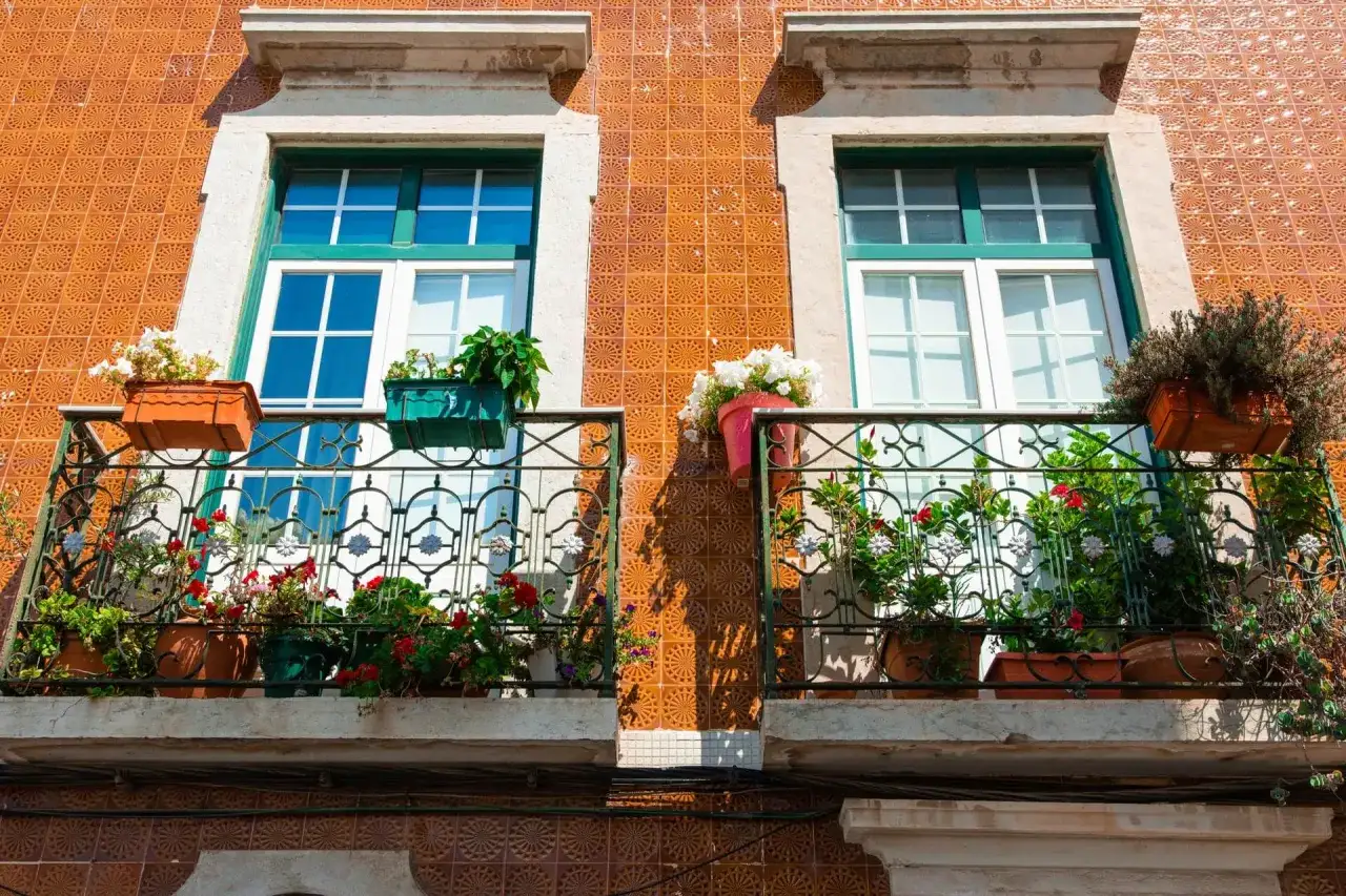 Dwa balkony z kwitnącymi kwiatami, ozdobione kafelkami. Czy balkon to część wspólna? Zależy od budynku, ale te wyglądają na prywatne.
