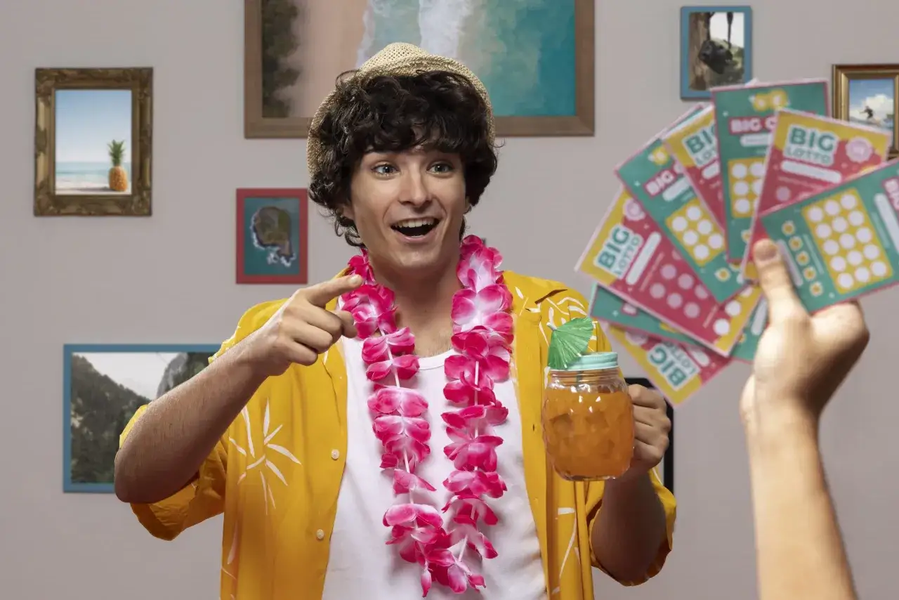 Uśmiechnięty mężczyzna w hawajskiej koszuli i naszyjniku z kwiatów trzyma drinka i zdrapki, sugerując, czy warto grać w zdrapki.