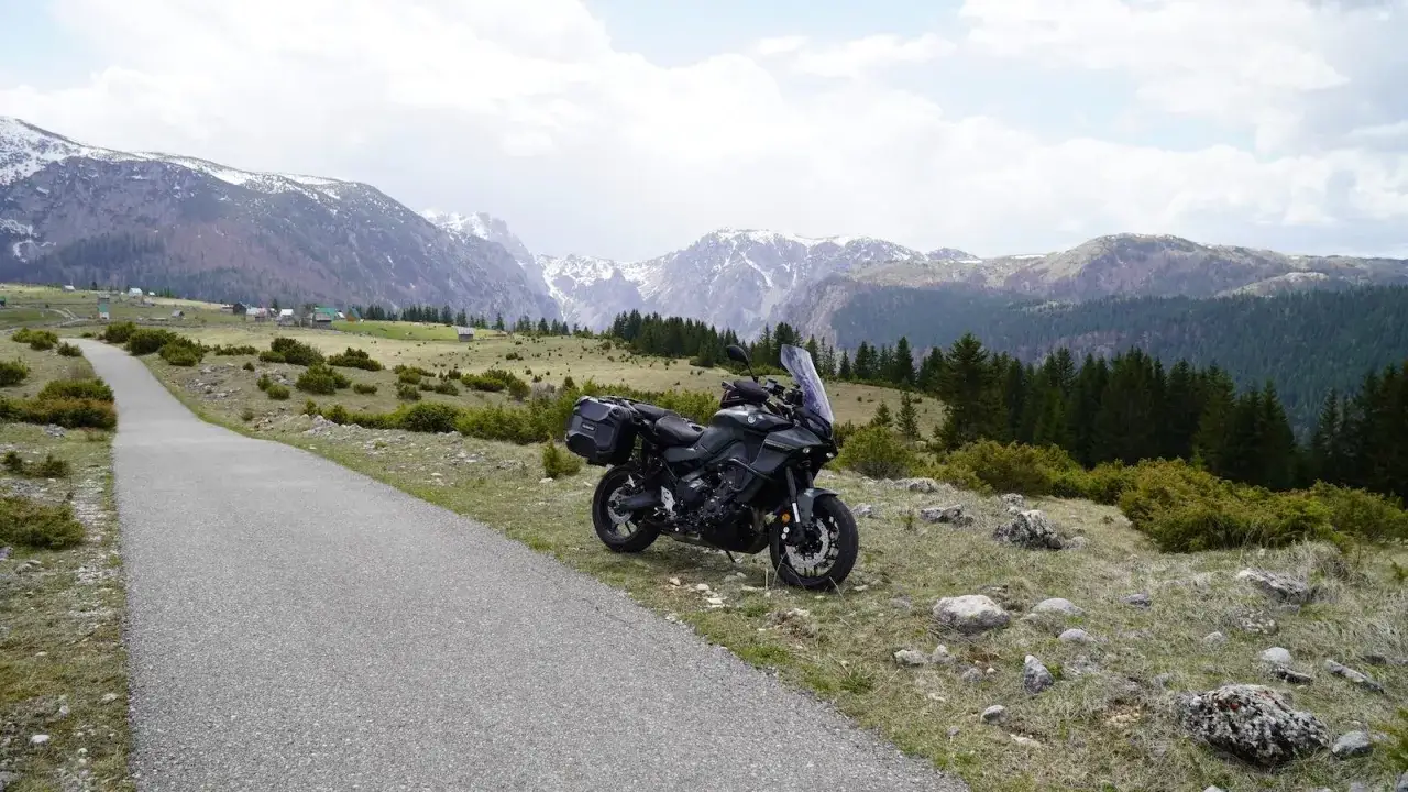Motocykl czeka na przygodę w Czarnogórze. Droga wije się wśród gór, lasów i małych domków.