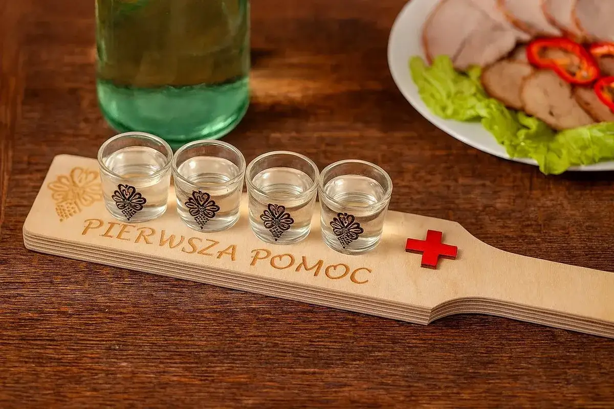 Cztery małe kieliszki z wódką na drewnianej desce z napisem 