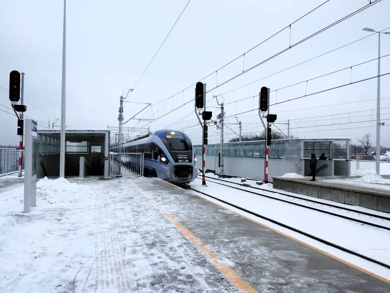Nowoczesny pociąg Białystok Warszawa zbliża się do stacji w zimowej scenerii.