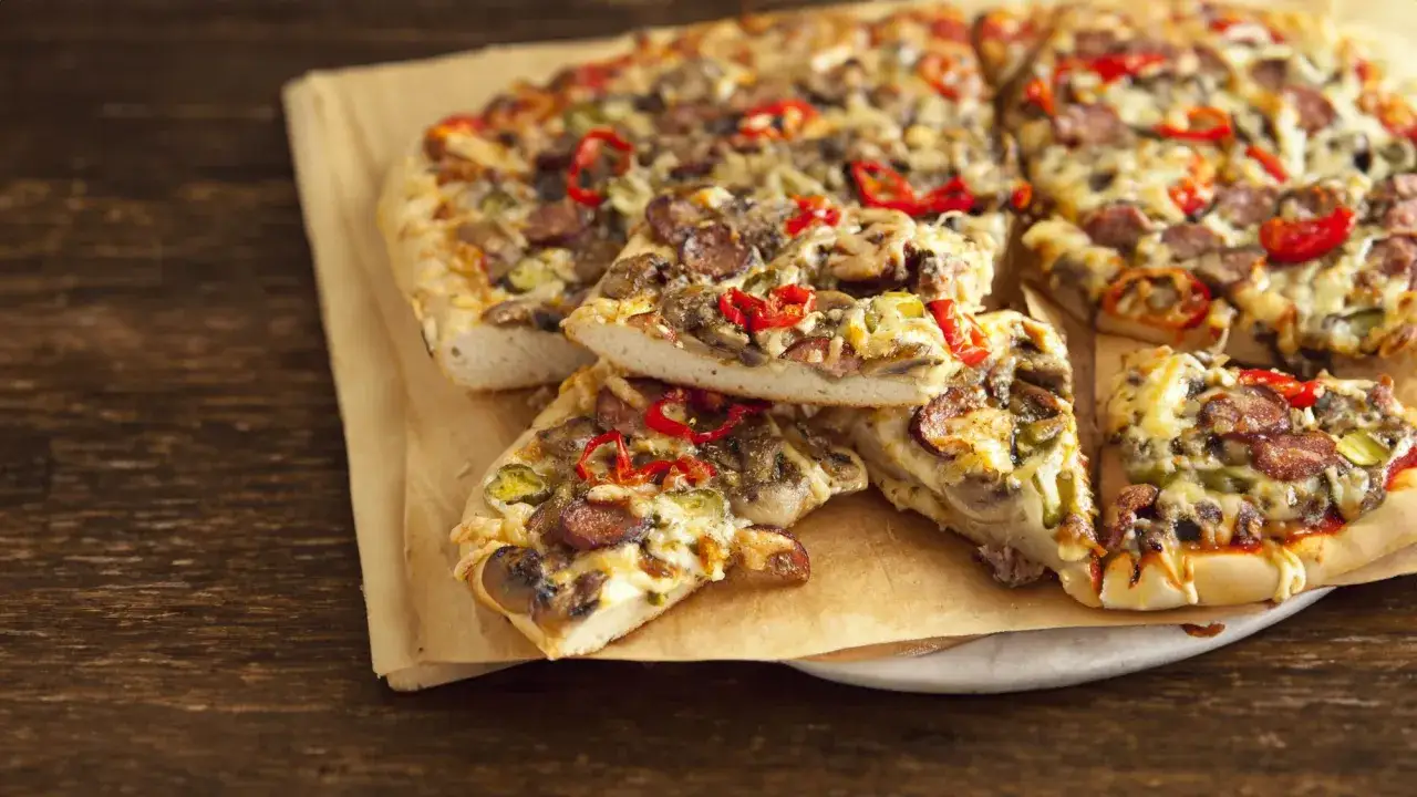 Grube ciasto na pizze z kiełbasą, pieczarkami i papryką, podane na papierze do pieczenia.