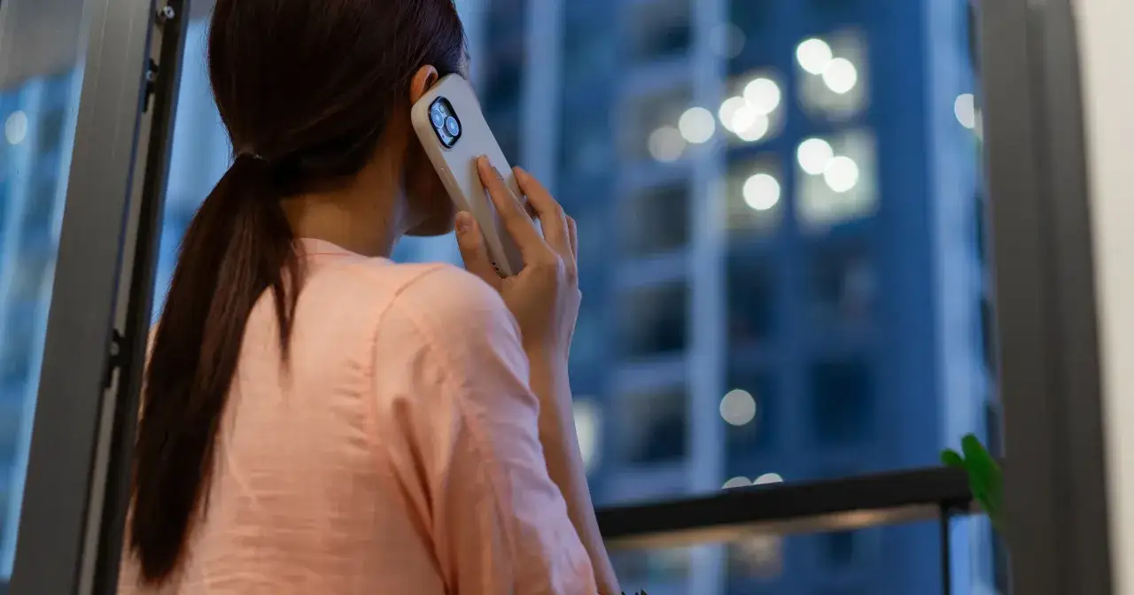 Dziewczyna rozmawia przez telefon, zastanawiając się, co napisać do dziewczyny wieczorem. W tle widać rozświetlone okna wieżowca.