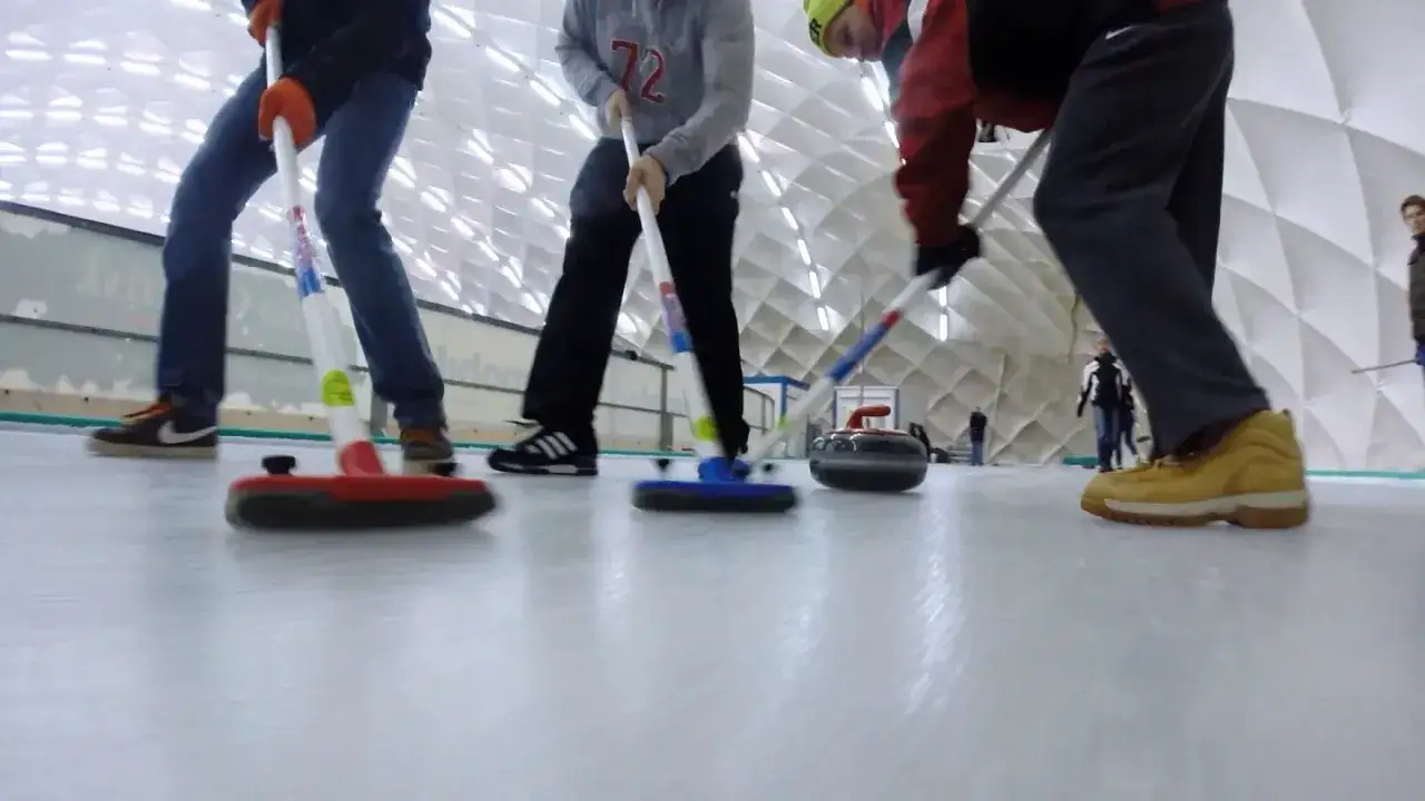 Gracze curlingu, dyscyplina sportowa na lodzie, szorują l&oacute;d miotłami, przygotowując się do rzutu kamieniem.