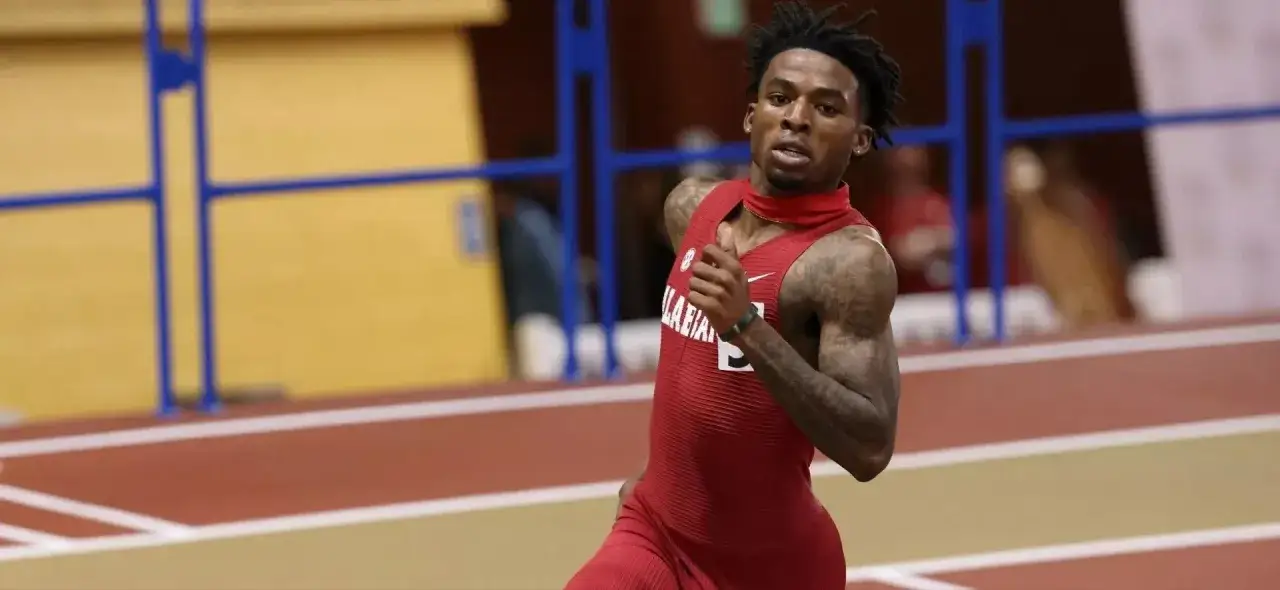 Sprinter w czerwonym stroju biegnie po bieżni, celując w rekord polski na 400 m mężczyzn.