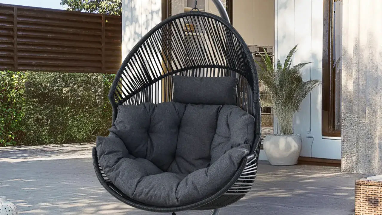 Czarny, wiszący fotel w kształcie kokonu z wygodnymi, szarymi poduszkami, idealny do relaksu na tarasie.