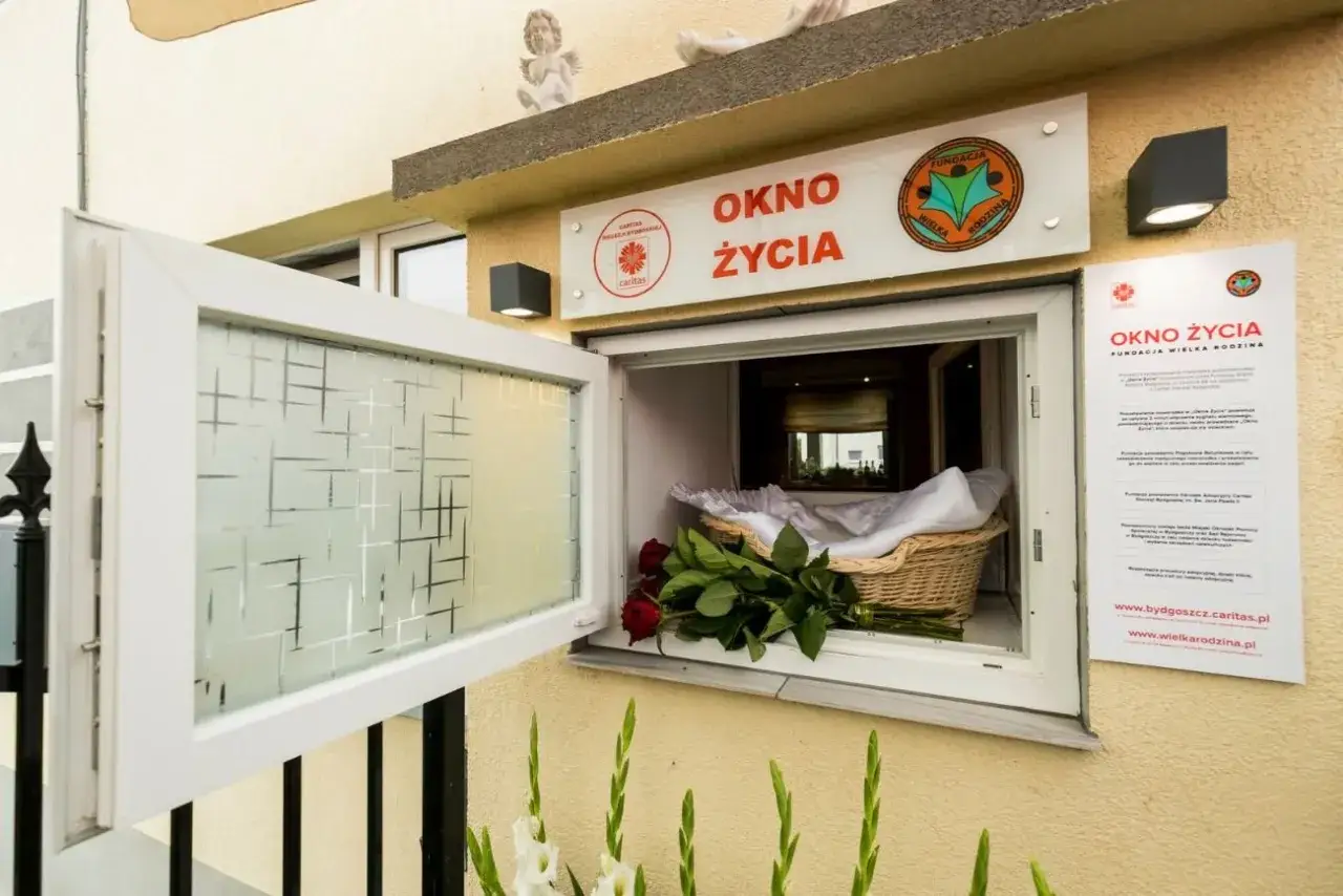 Okno życia z koszykiem, białym kocykiem i czerwonymi różami. To miejsce nadziei dla noworodków.