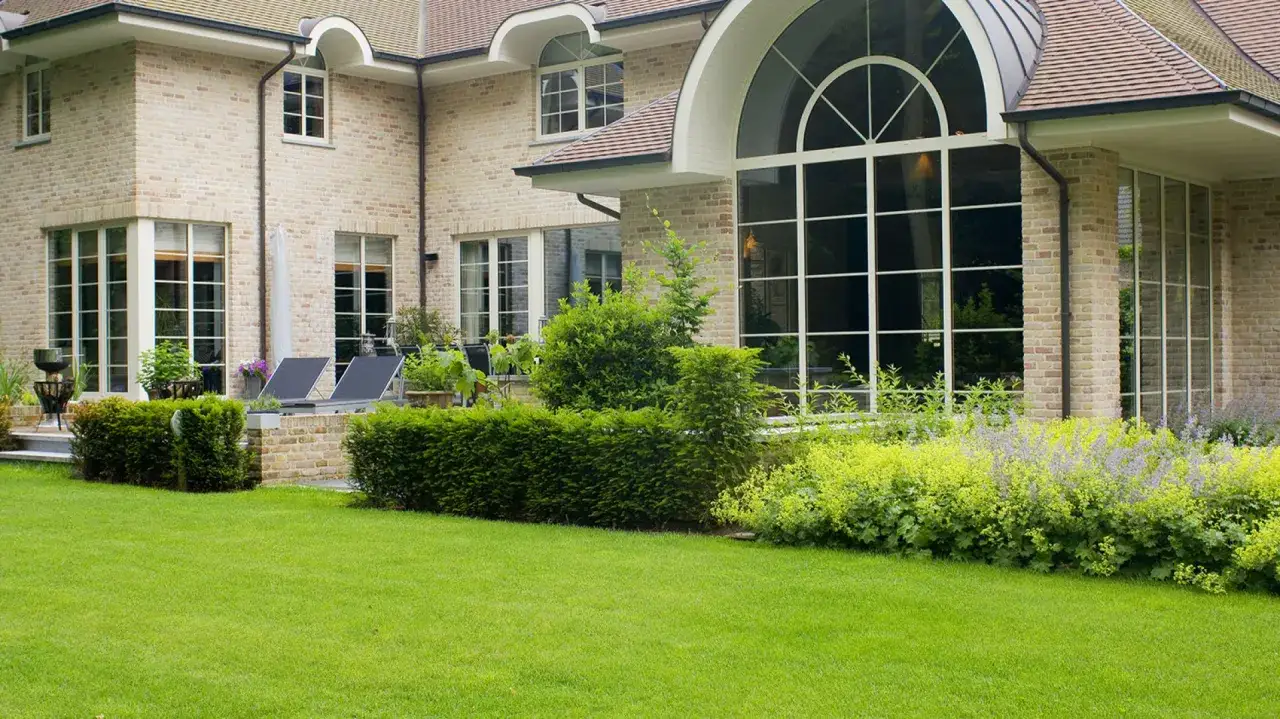 Elegancka willa z cegły, z pięknymi **oknami ze szprosami**, otoczona zadbanym ogrodem i trawnikiem.