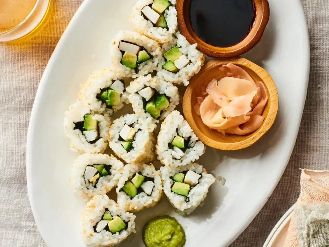 Talerz pełen świeżego california roll sushi z awokado i paluszkami krabowymi, podany z imbirem i wasabi.