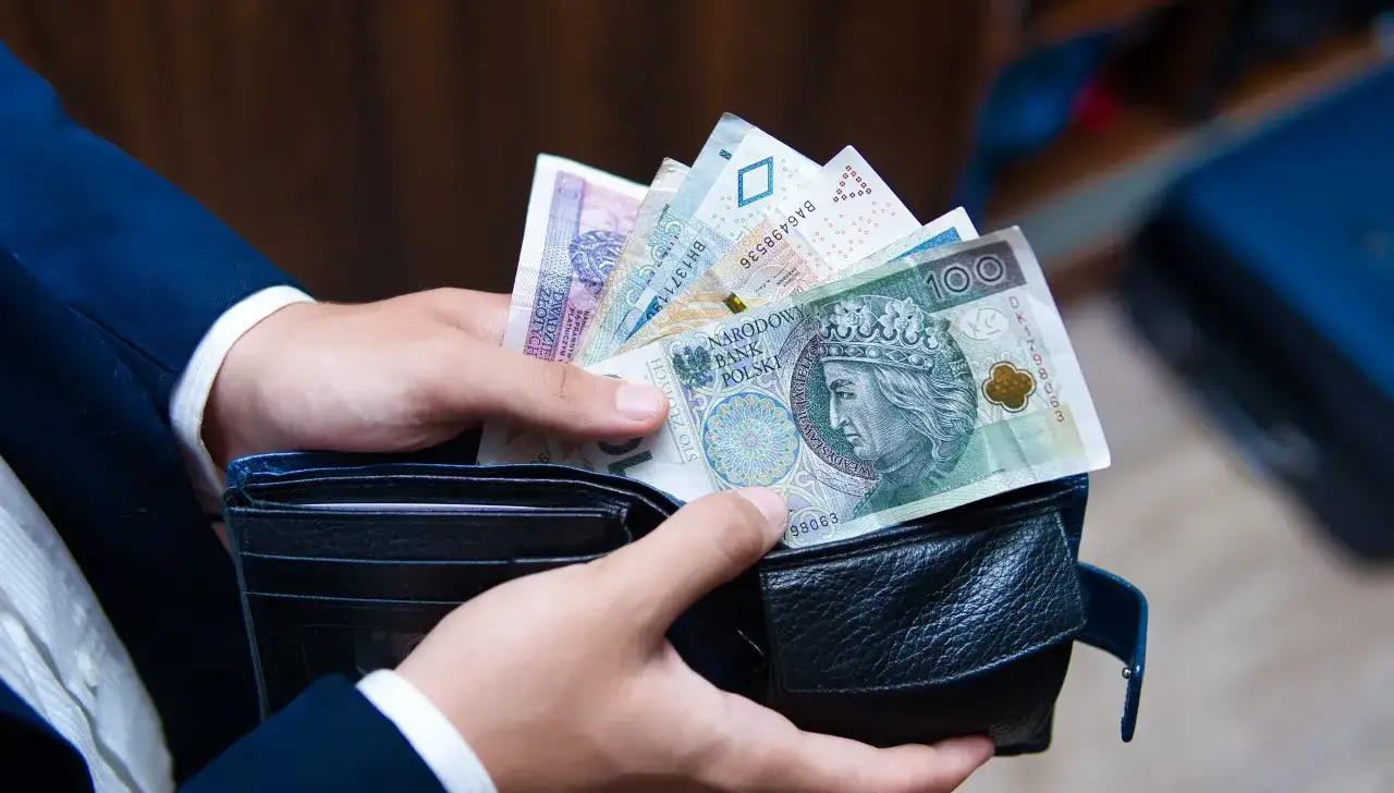 Ręce wkładają polskie banknoty do portfela. Nowa praca to szansa na lepszą przyszłość i stabilność finansową, a PPK może pomóc w jej budowaniu.