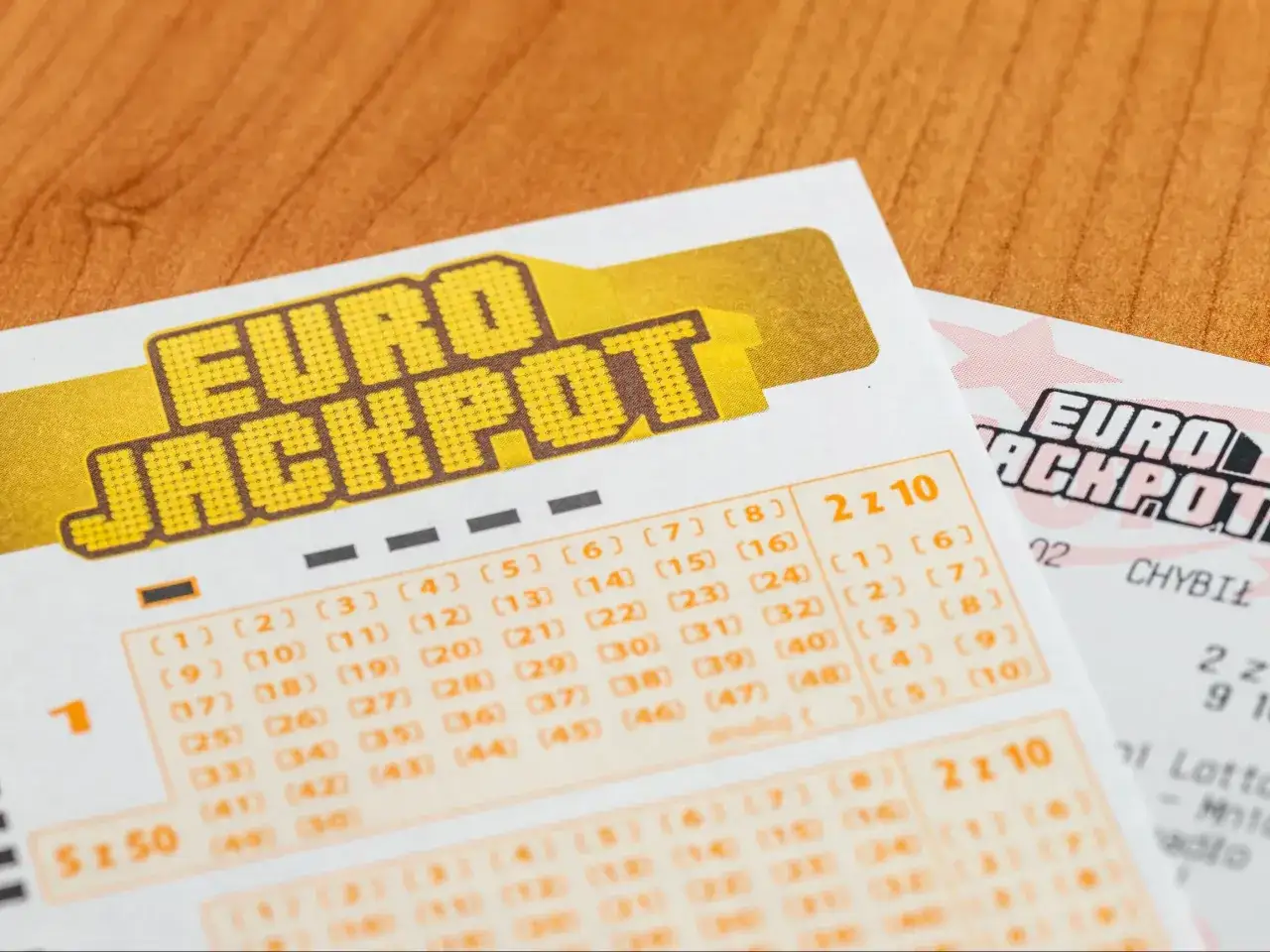 Kupony Eurojackpot Polska na drewnianym stole. Widoczne pola do zaznaczenia liczb i logo gry.
