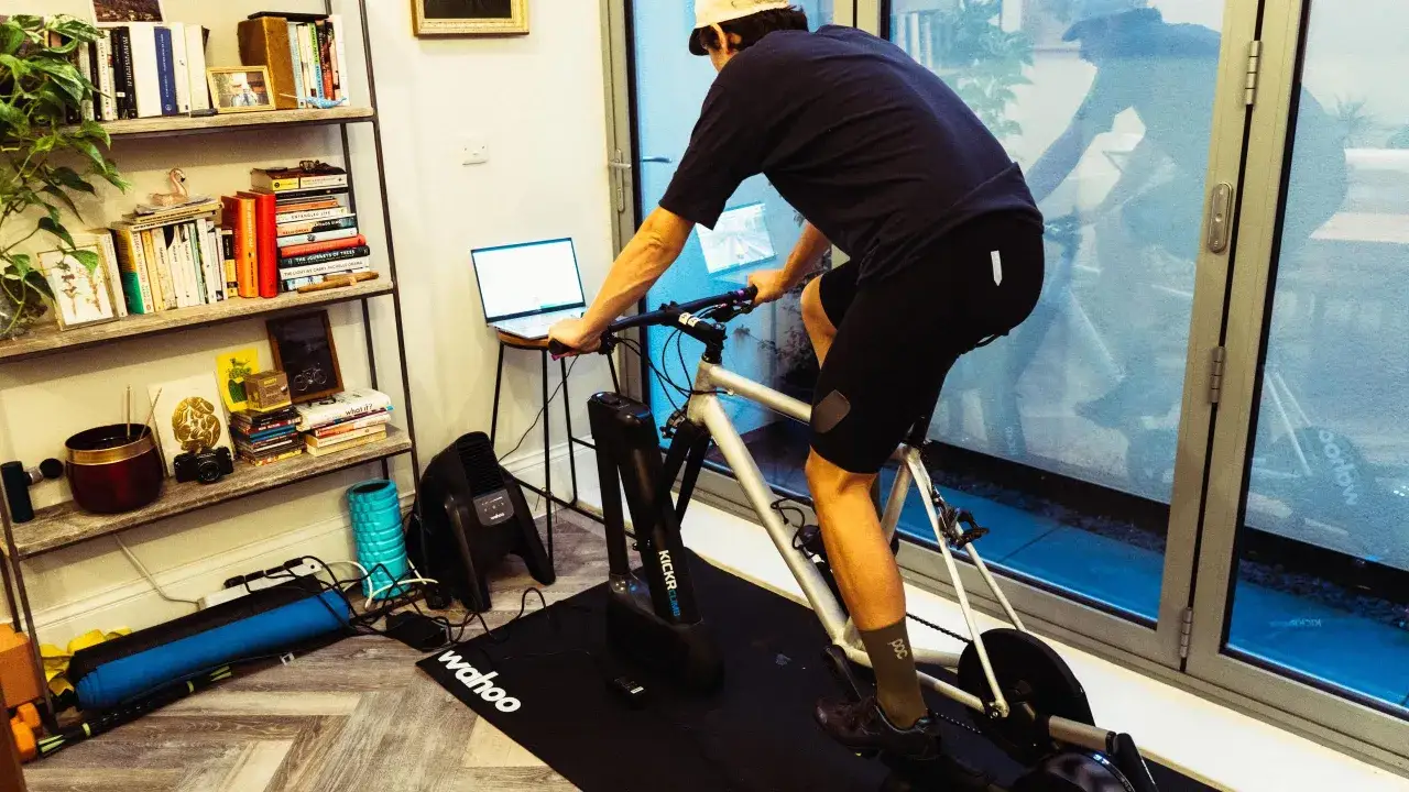 Mężczyzna na rowerze stacjonarnym, realizując sw&oacute;j trening rowerowy plan, z laptopem obok.