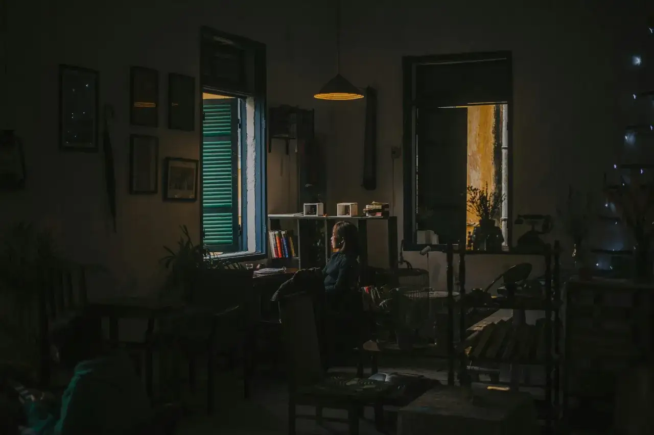 Kobieta siedzi przy oknie, wpatrując się w światło. W pokoju panuje p&oacute;łmrok, jak w ciemni fotograficznej, gdzie powstaje roztw&oacute;r.