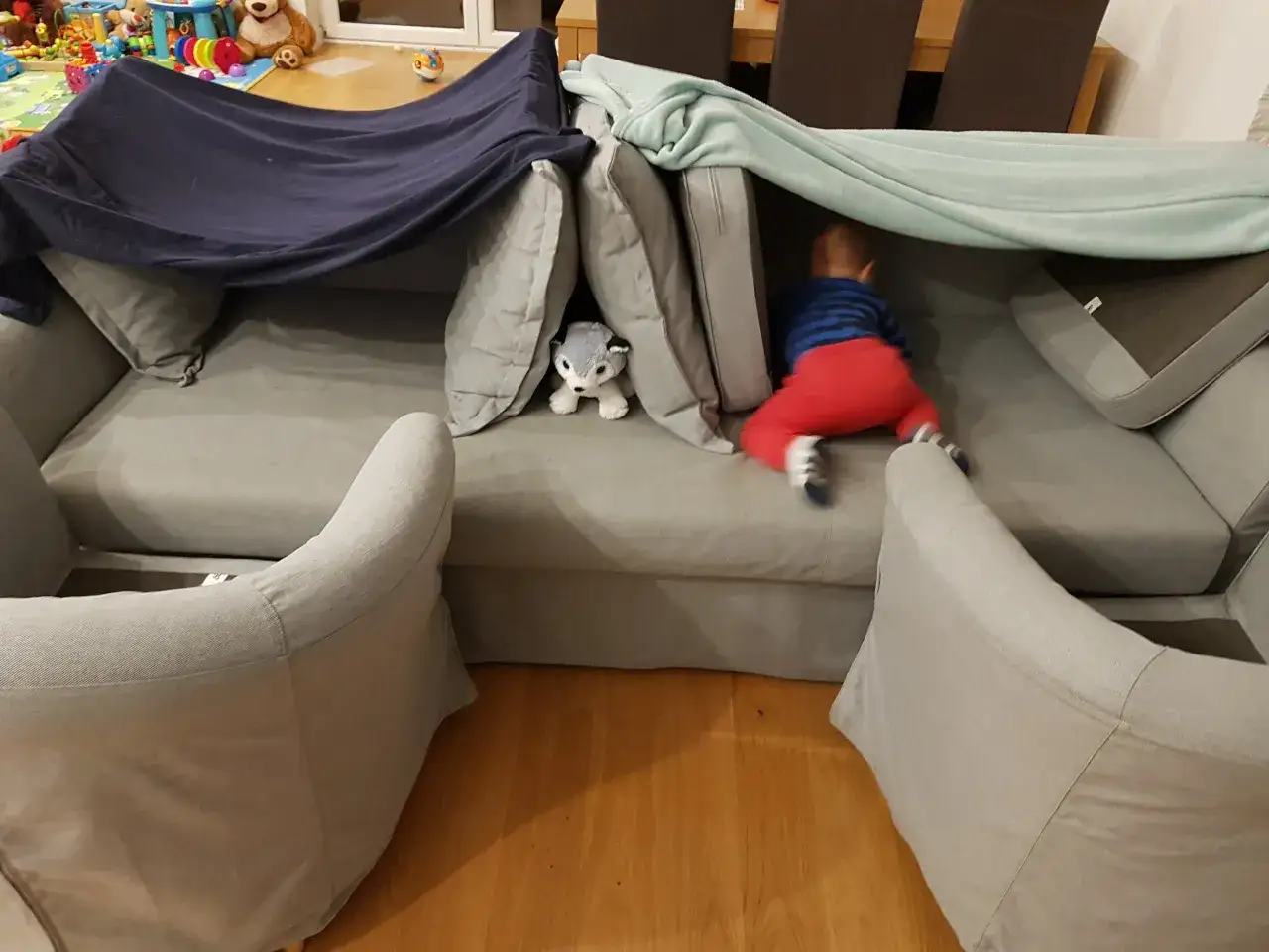 Dziecko w czerwonych spodniach czołga się do przytulnej bazy z kocy i poduszek.