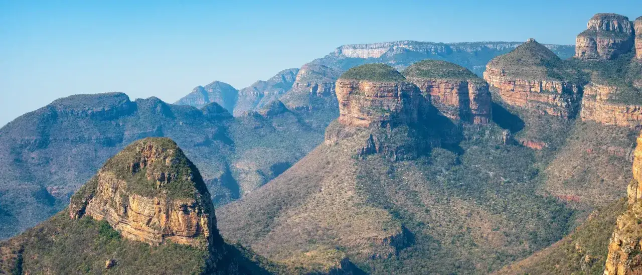Imponujące g&oacute;ry przylądkowe o stożkowatych szczytach, porośnięte zielenią i skaliste, w blasku słońca.