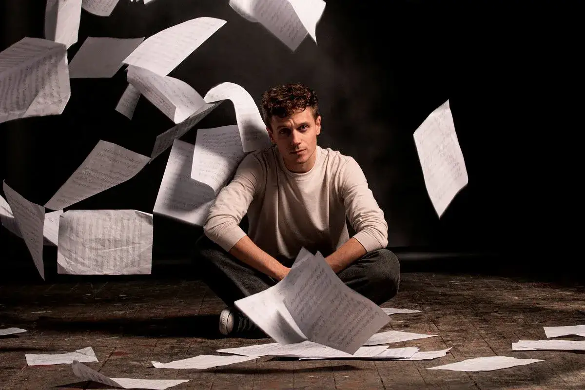 Młody mężczyzna siedzi na podłodze wśród fruwających kartek z nutami. Czas ucieka, tik tik bum, a on wpatruje się w przestrzeń. Roma.