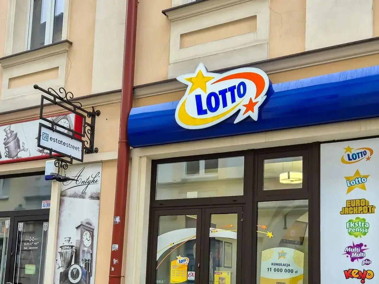 Logo LOTTO nad wejściem do punktu sprzedaży. Tutaj dowiesz się, jak sprawdzać lotto z plusem i wygrać!