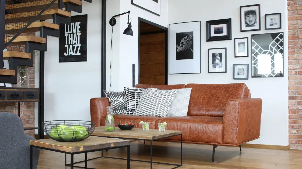 Jak powiesić obraz na ścianie? W salonie z brązową kanapą, schodami i galerią zdjęć.