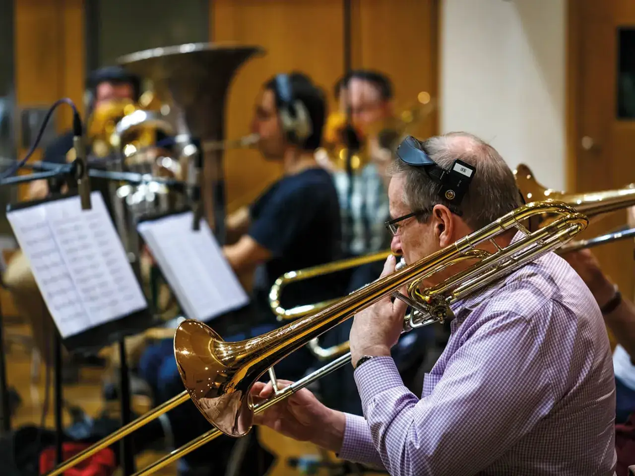 Orkiestra gra na instrumentach dętych. Muzycy w słuchawkach ćwiczą przed nagraniem.