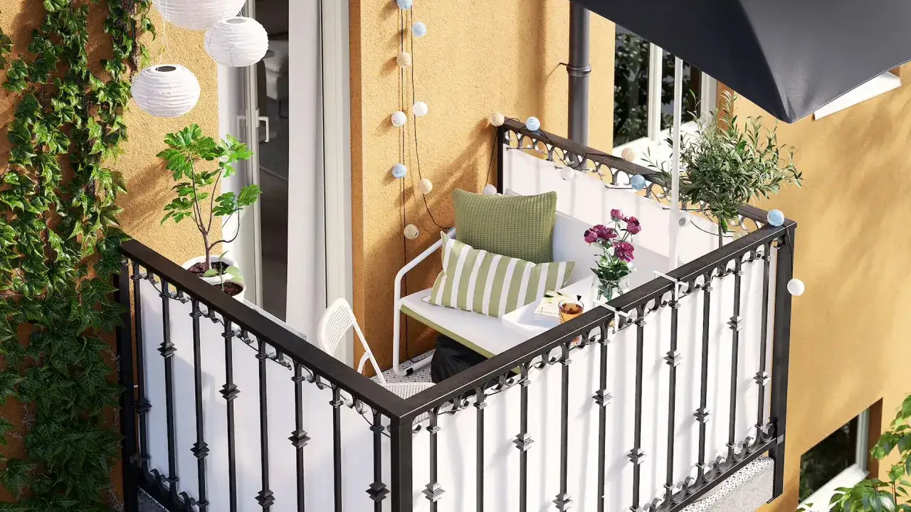 Przytulny mały balkon w bloku z zieloną roślinnością, wygodną ławką i ozdobnymi lampkami. Idealne miejsce na poranną kawę.