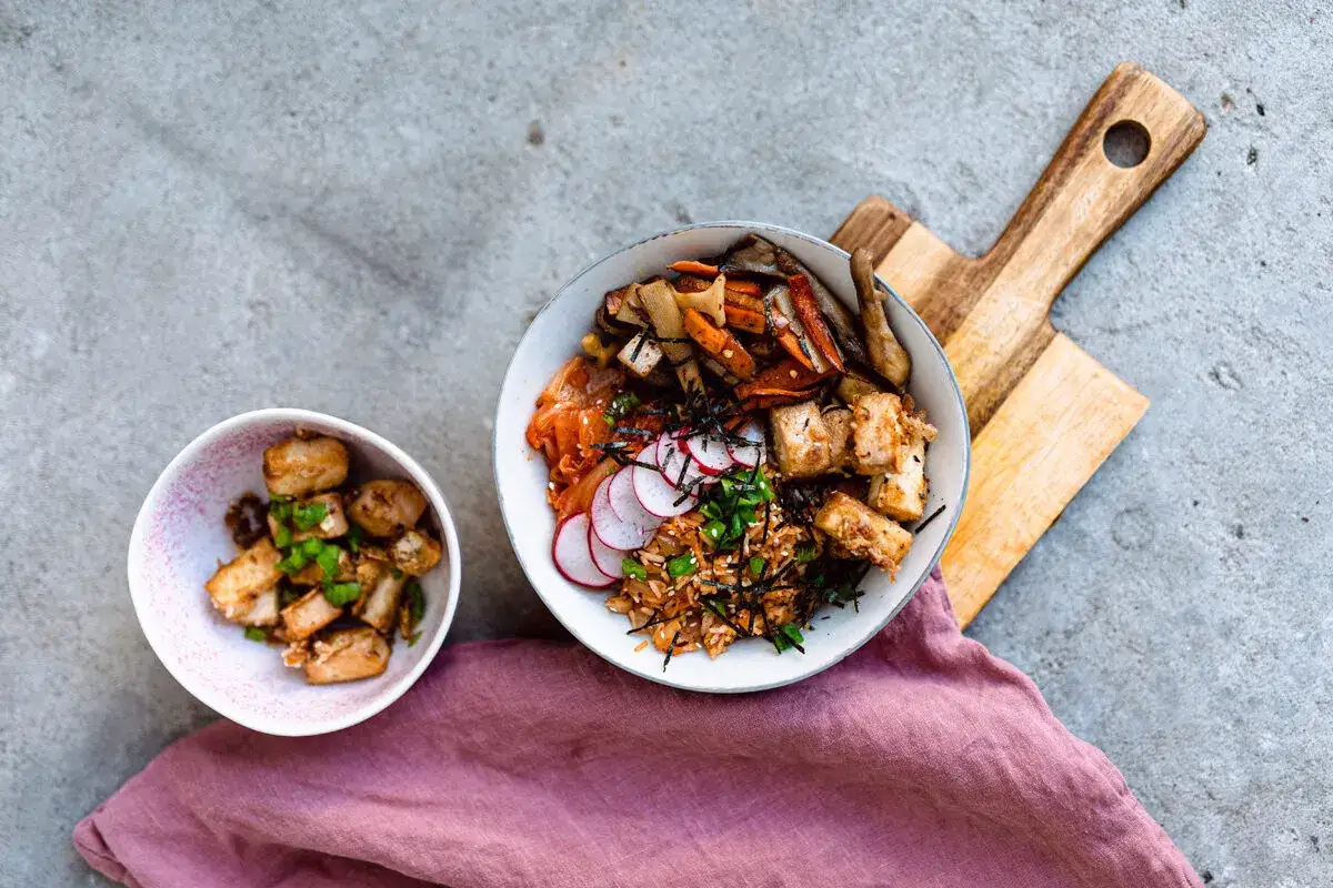 Dwa miseczki z daniami. Jedna z ryżem, kimchi, rzodkiewką i pieczonym tofu. Druga z pieczonym tofu i szczypiorkiem. Idealne na dieta wegańska co jeść.