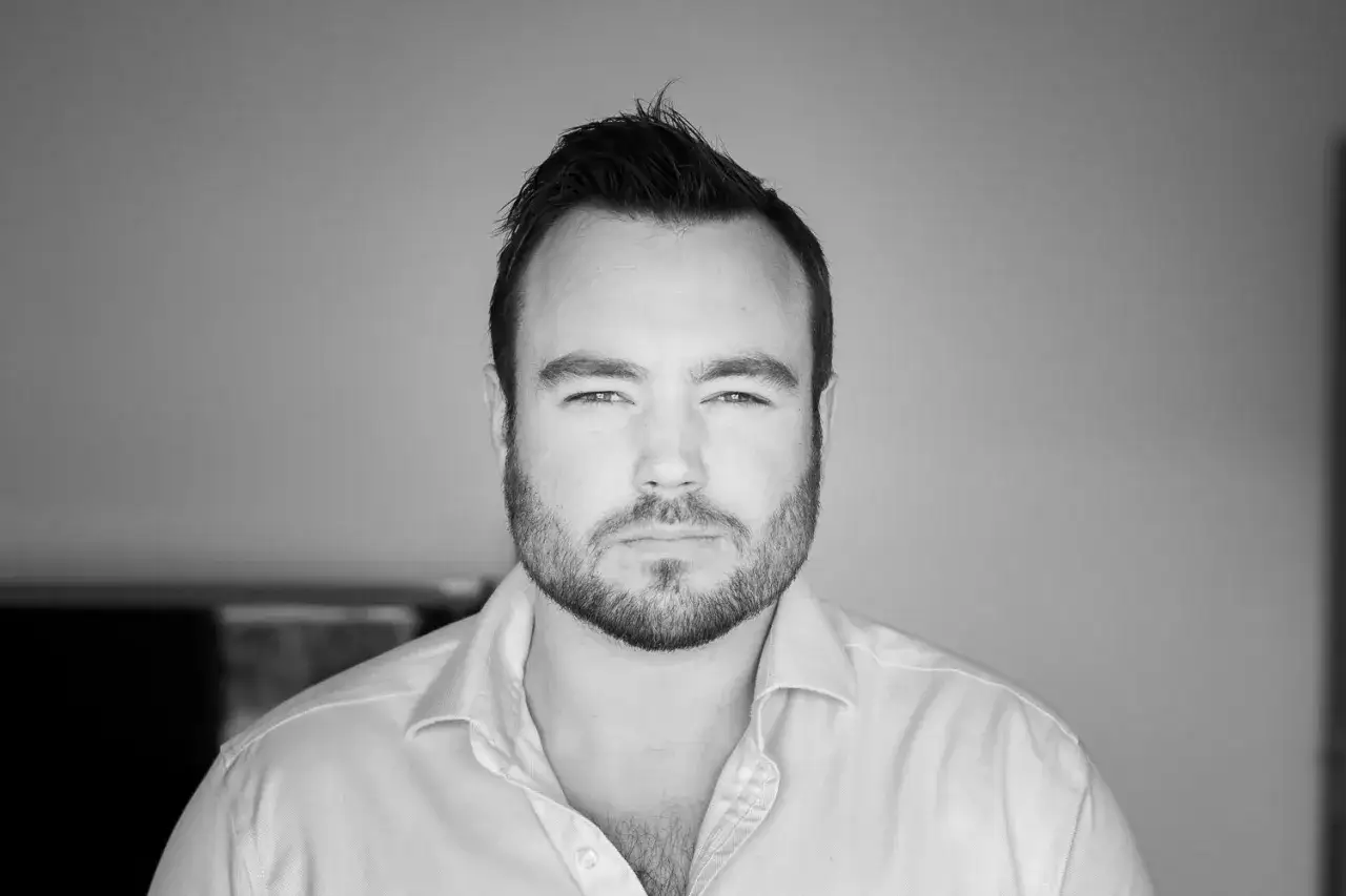 Męskie zdjęcie profilowe: młody mężczyzna z zarostem, w białej koszuli, patrzy prosto w obiektyw.