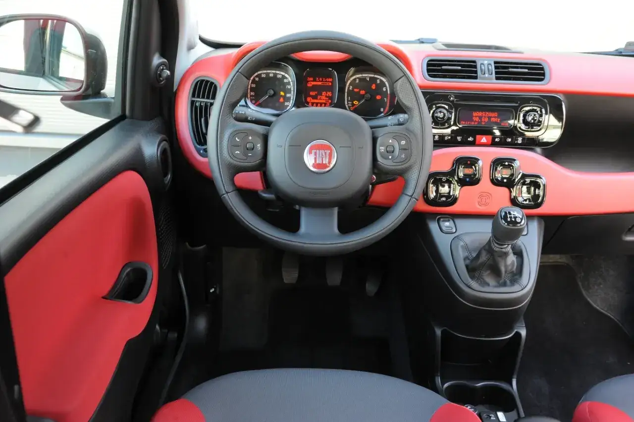 Wnętrze Fiata Panda automat z czerwonymi akcentami. Kierownica, deska rozdzielcza i fotel kierowcy.