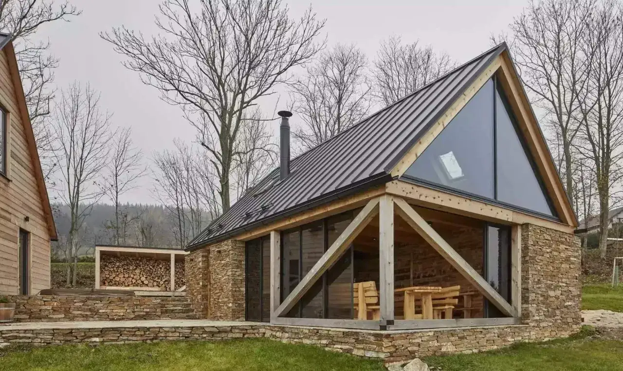 Nowoczesne domy z drewna i szkła, z kamienną podstawą i dużymi przeszkleniami, w otoczeniu nagich drzew.