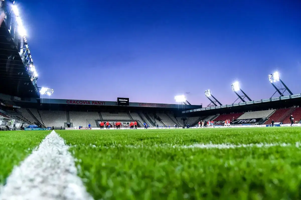 Piłkarze na murawie stadionu Cracovii. Widać trybuny, oświetlenie i napis 