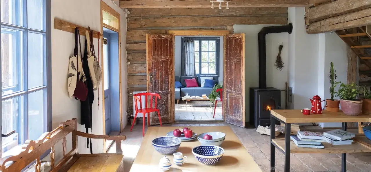Wnętrze drewnianego domu po remoncie: piec, st&oacute;ł z misami, kanapa w salonie.