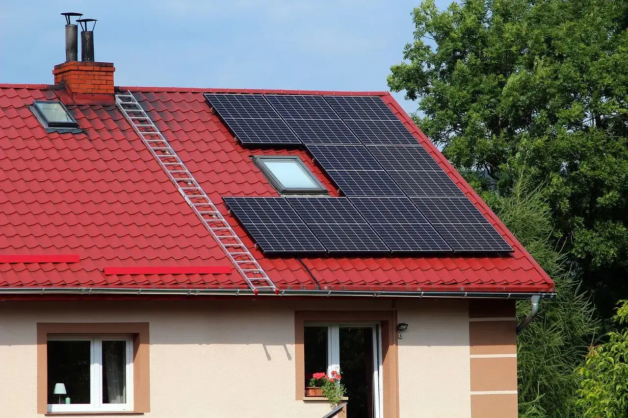Nowy dom z instalacją off grid. Panele słoneczne na czerwonym dachu, drabina prowadząca do komina.