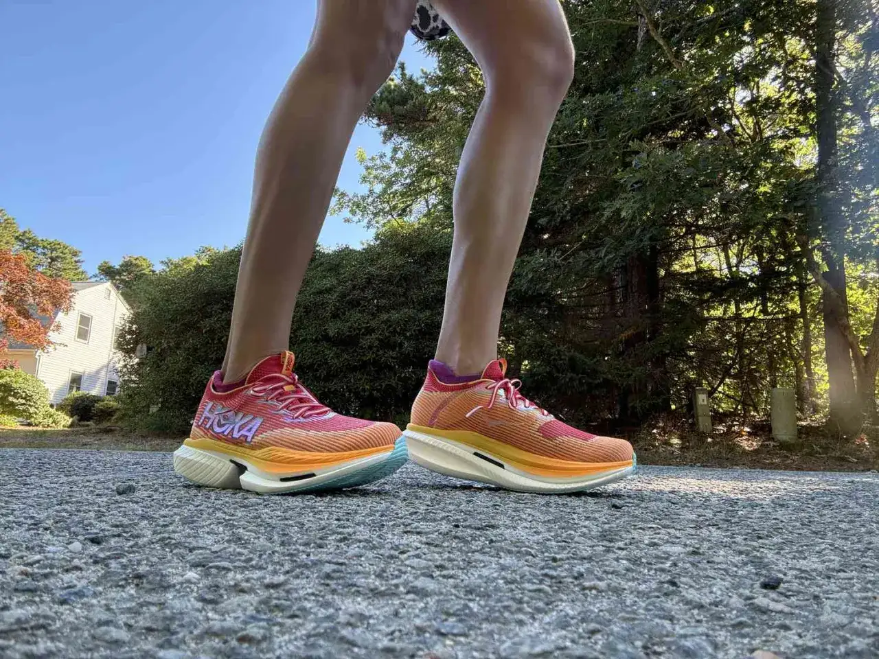 Kolorowe buty do maratonu Hoka na nogach biegacza na tle zieleni i błękitnego nieba.