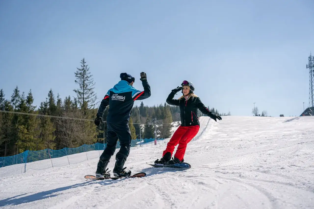 Instruktor i kursantka cieszą się udaną nauką jazdy na snowboardzie. Dają sobie 