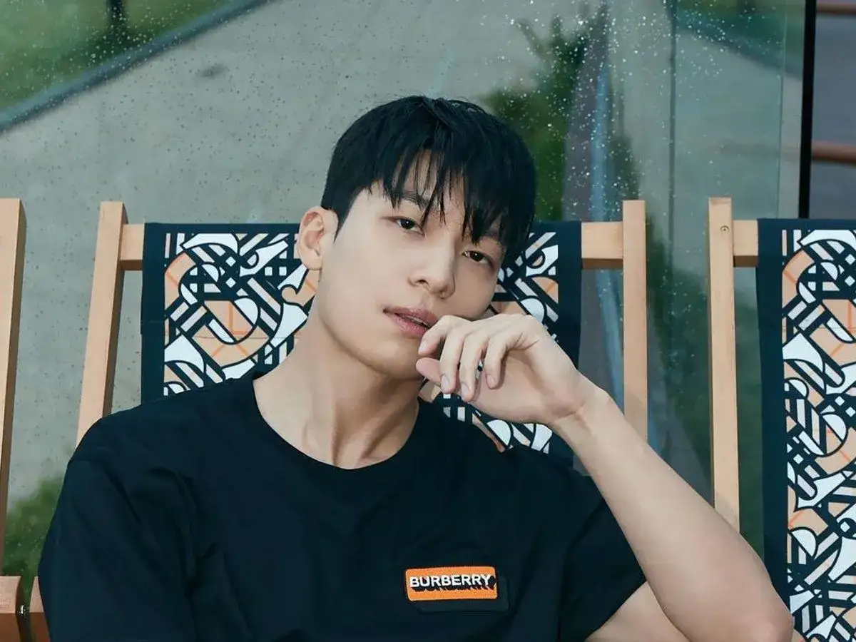 Wi Ha-joon w czarnej koszulce Burberry, siedzi na krześle z charakterystycznym wzorem. Jego filmy i seriale cieszą się popularnością.